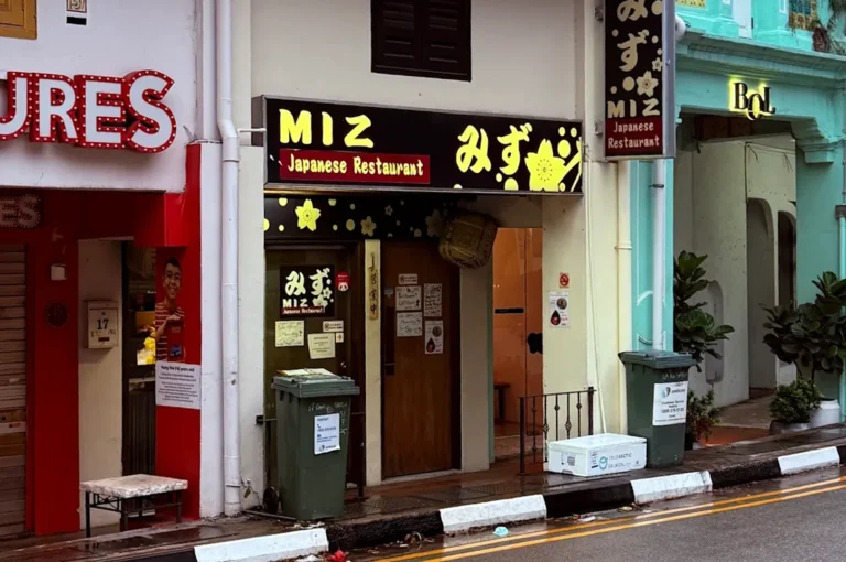 The traditional shophouse entrance of MIZ Japanese Restaurant with a black and yellow sign featuring cherry blossom motifs.