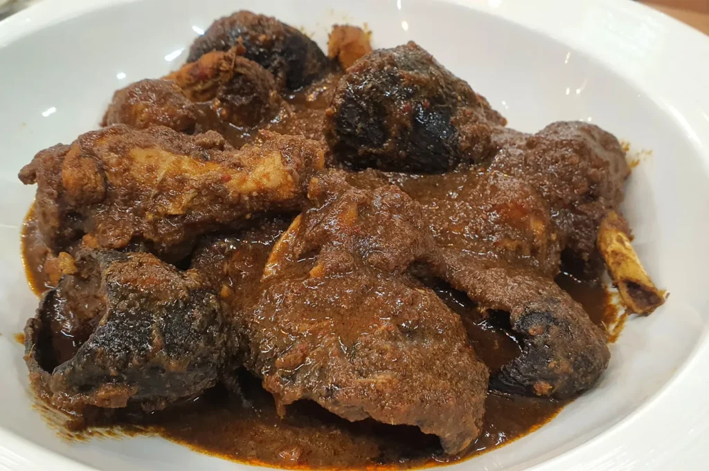 A close-up view of Ayam Buah Keluak, a traditional Peranakan chicken stew with black nuts in a rich gravy.
