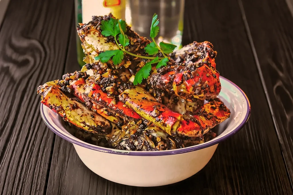 A bowl of spicy cooked crab legs coated in black pepper sauce, garnished with fresh cilantro, sits on a dark wooden table, conveying a savory and appetizing tone.