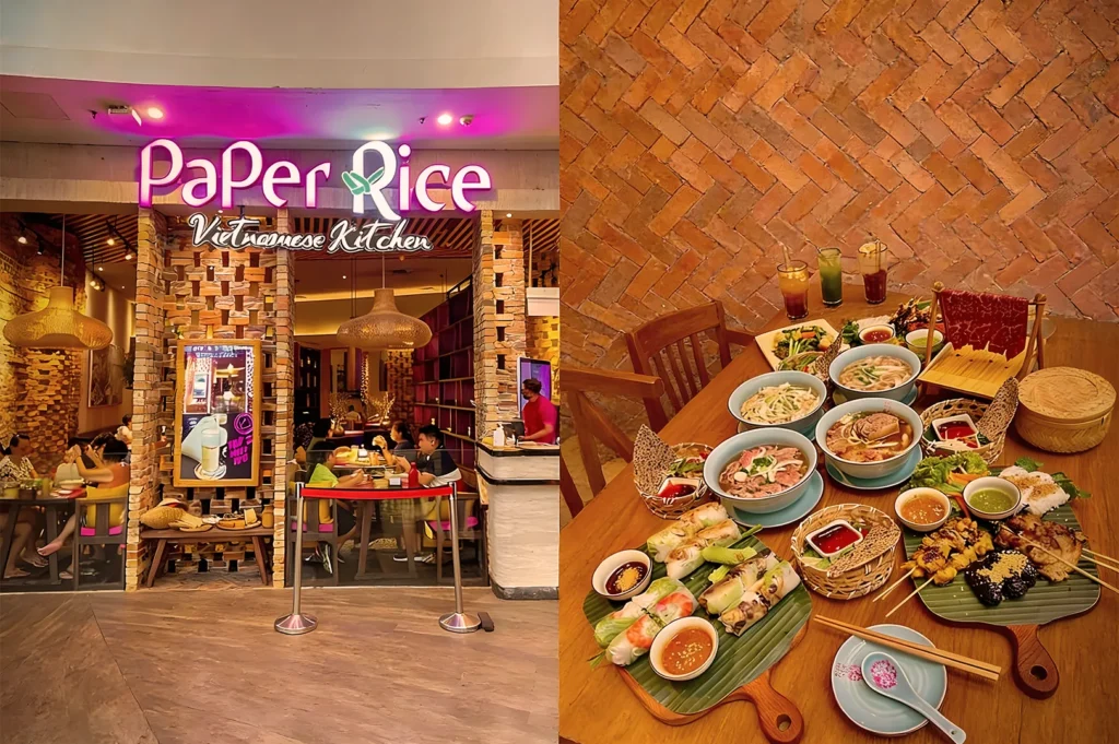 Storefront of "Paper Rice Vietnamese Kitchen," warmly lit with diners inside. Nearby, a table laden with vibrant Vietnamese dishes and drinks on a brick background.
