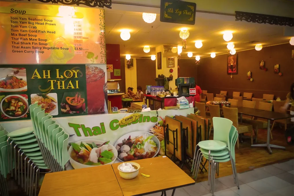Interior of Ah Loy Thai restaurant showing a large menu board, traditional Thai decor, and neatly arranged dining tables and chairs.