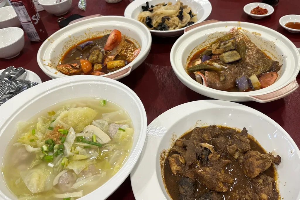 A spread of authentic Peranakan dishes including Assam Fish, Chap Chye, and Bakwan Kepeting soup on a dining table.