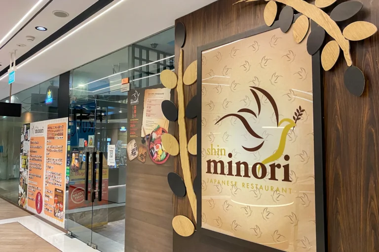 Entrance to Shin Minori Japanese Restaurant featuring a wooden wall with their bird logo and a menu board showing sushi buffet options.