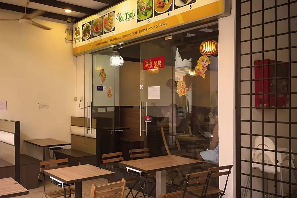 Jai Thai restaurant entrance in Singapore, displaying a modern glass facade, outdoor wooden tables, and traditional lanterns.