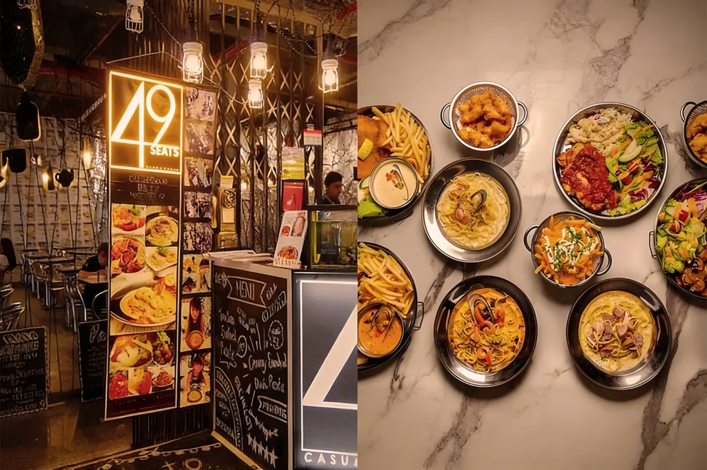 Cozy restaurant entrance with warm lighting and food photos, leading to seating beneath hanging lights. On the side, dishes with pasta, salads, fries, and sauce are beautifully plated on a marble table.