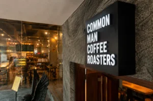 Common Man Coffee Roasters black illuminated sign on textured exterior wall
