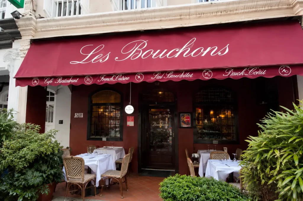 Exterior view of Les Bouchons restaurant featuring a burgundy awning and outdoor dining tables with white tablecloths