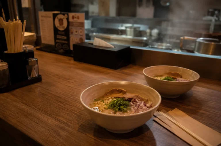 Two bowls of ramen with meat and green onions on a wooden counter