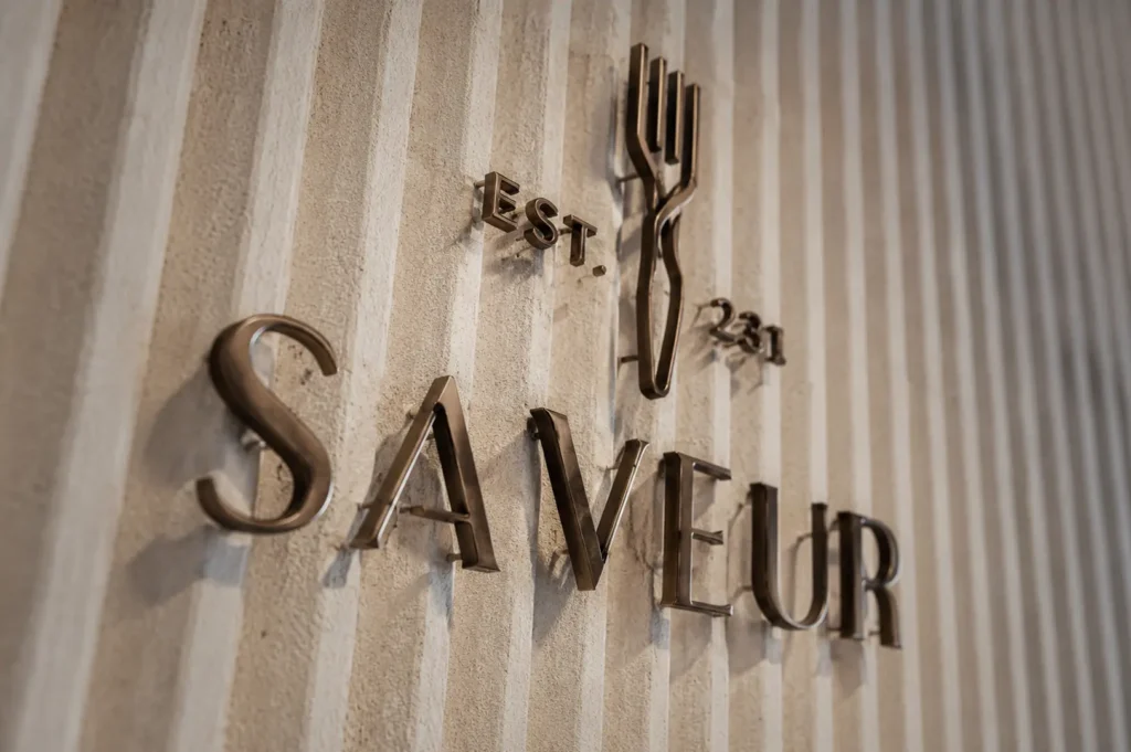 Metallic 3D Saveur restaurant logo and signage mounted on a textured white wall