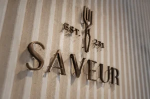 Metallic 3D Saveur restaurant logo and signage mounted on a textured white wall