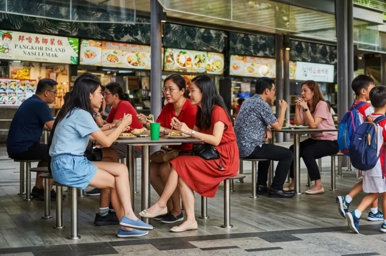 Groups of people dining and socializing at tables in a modern hawker centre with Nasi Lemak stall signage
