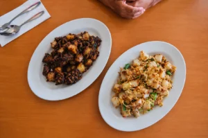 Two plates of Singaporean fried radish cake showing dark and white variations with eggs on a wooden table