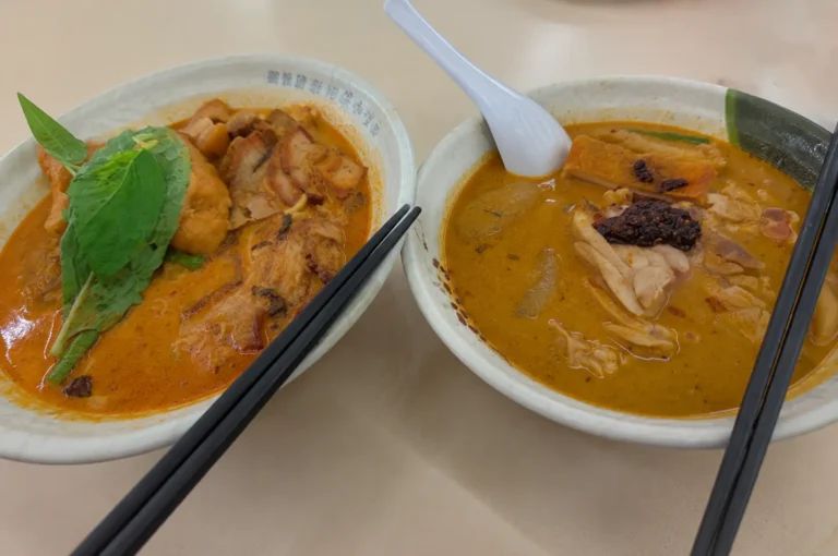 Two bowls of Singapore soup curry served side by side on a casual dining table, captured from a natural phone side angle