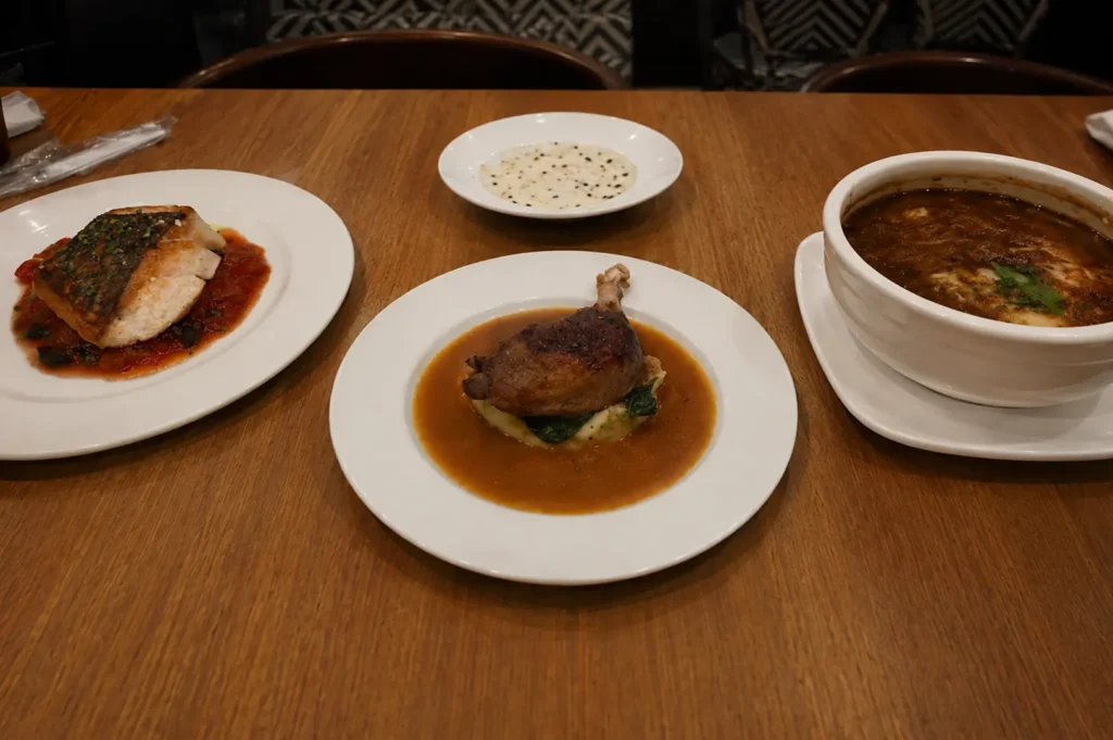 Wooden table set with classic French dishes including duck confit, seared fish, and French onion soup