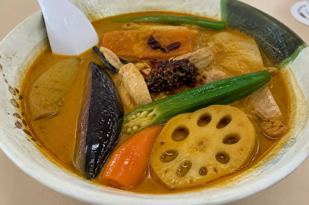 Close-up of a Singapore soup curry with lotus root, okra, eggplant, carrot, and rich spiced broth in a ceramic bowl