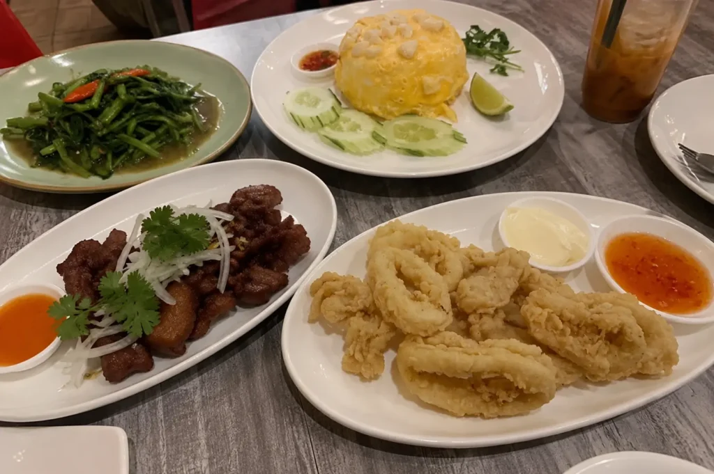 Table spread of Thai dishes including crab omelette, fried calamari, morning glory, and fried meat with dipping sauces