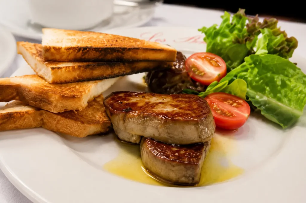 Close-up of seared foie gras served with toasted bread and a side salad on a white plate