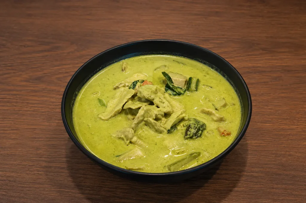 Green chicken curry with vegetables and Thai basil in black bowl