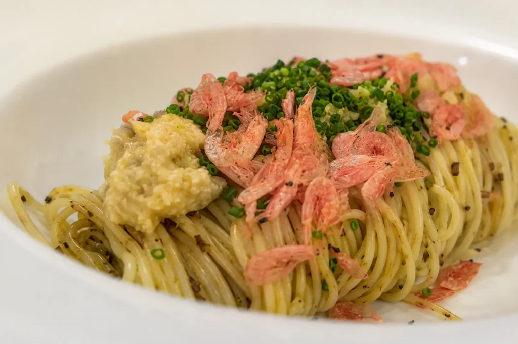 Close-up of angel hair pasta topped with small pink dried shrimp, chopped chives, and garlic paste