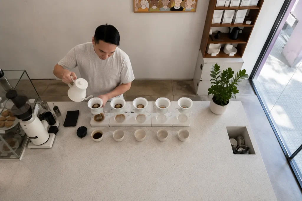 Barista preparing multiple pour-over coffees in a row on a white counter