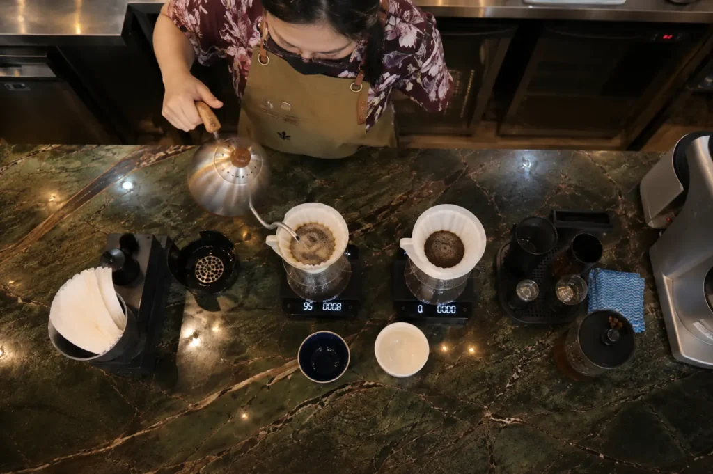 Barista preparing pour-over coffee with gooseneck kettle and digital scales at marble counter