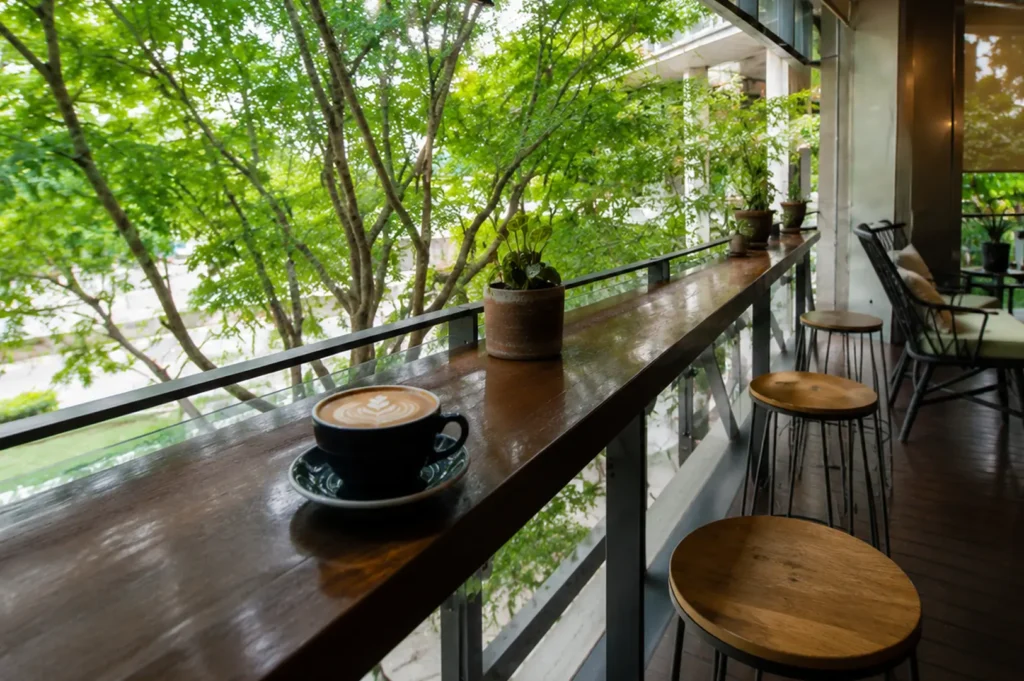 Coffee cup with latte art on wooden counter overlooking lush green trees from balcony seating