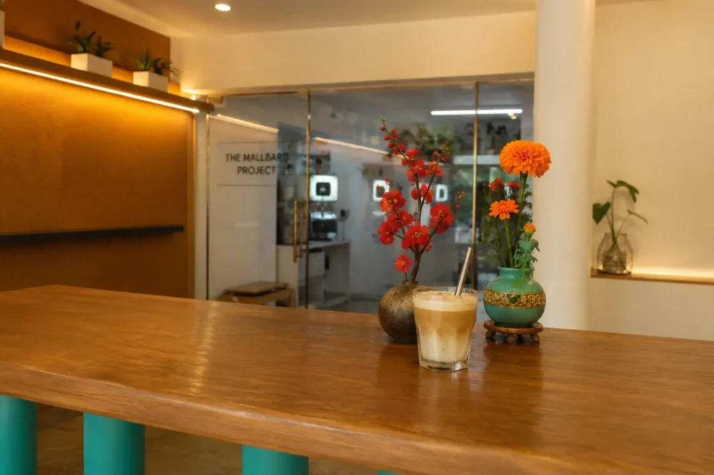 Iced coffee on wooden table with colorful flower vases at Nylon Coffee Roasters, with modern cafe interior visible in background