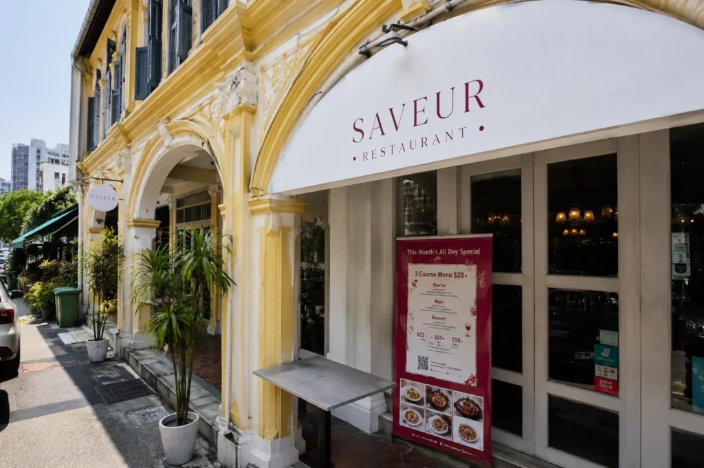 Exterior of Saveur Restaurant showing a classic colonial shophouse facade with a white awning and menu board