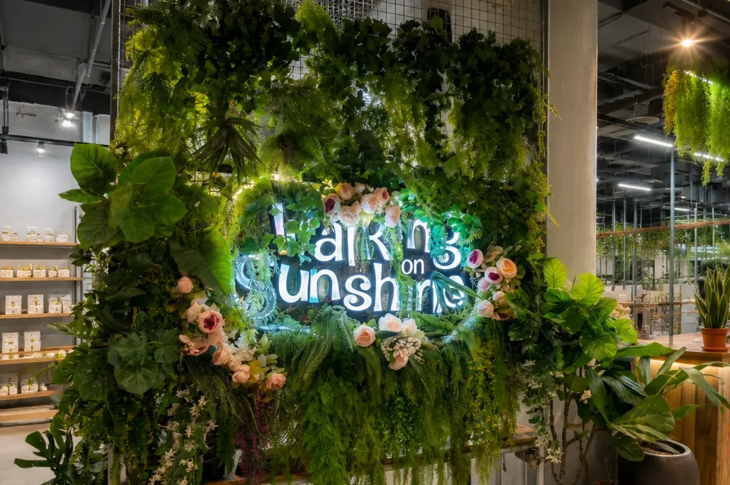 Lush greenery wall display framing a neon "Walking on Sunshine" sign in a modern space