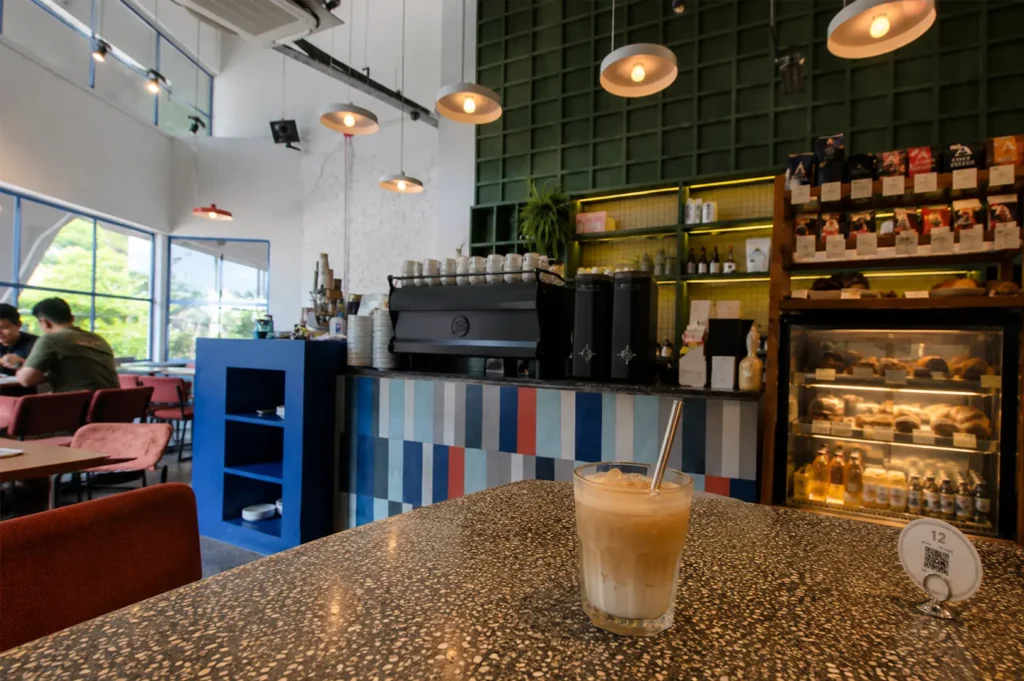 Colorful interior of Atlas Coffeehouse showing a striped counter, espresso machine, pastry display, and an iced coffee on a terrazzo table