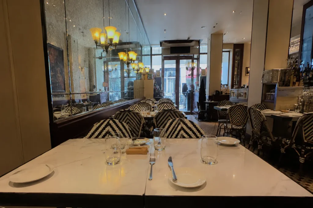 Classic French bistro interior with marble tables, black and white chevron chairs, and mirrored walls