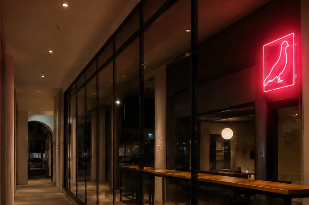 Modern restaurant exterior at night featuring large glass windows and a glowing red neon pigeon sign
