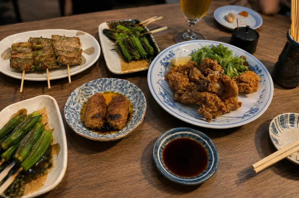Izakaya table spread with yakitori skewers, grilled vegetables, karaage fried chicken, and meatballs