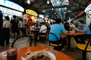 People dining and queuing for food inside a bustling hawker centre with multiple local food stalls