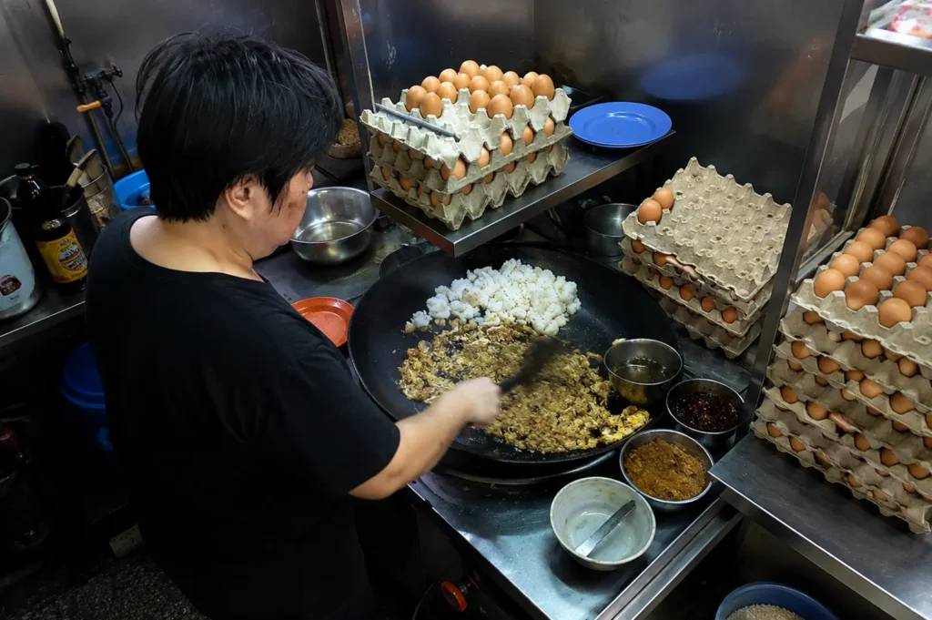 Hawker cook stir-frying fried rice with eggs and seasonings at a busy street food stall