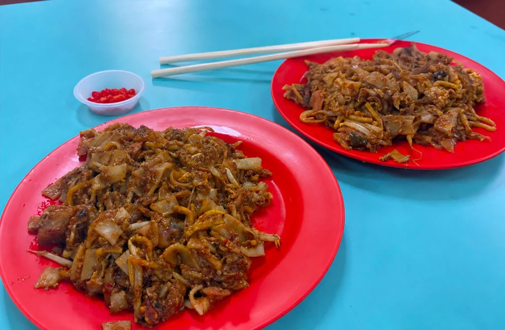 Plates of wok-fried hawker noodles served with fresh chili at a Singapore food centre.