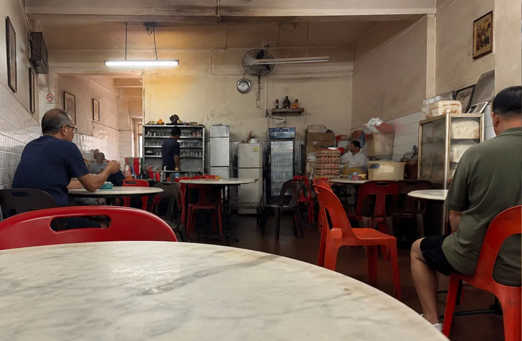Interior of a traditional Singapore kopitiam with diners and tables.