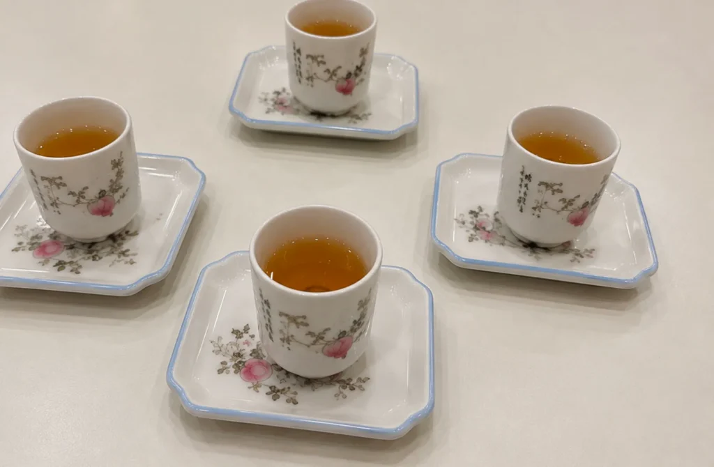 Four porcelain teacups filled with freshly brewed Chinese tea, served on matching floral saucers for a traditional tea tasting
