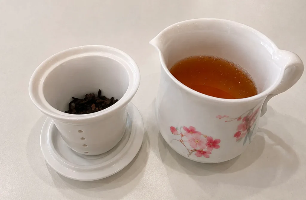 Freshly brewed Oolong tea poured into a porcelain serving pitcher beside steeped tea leaves.